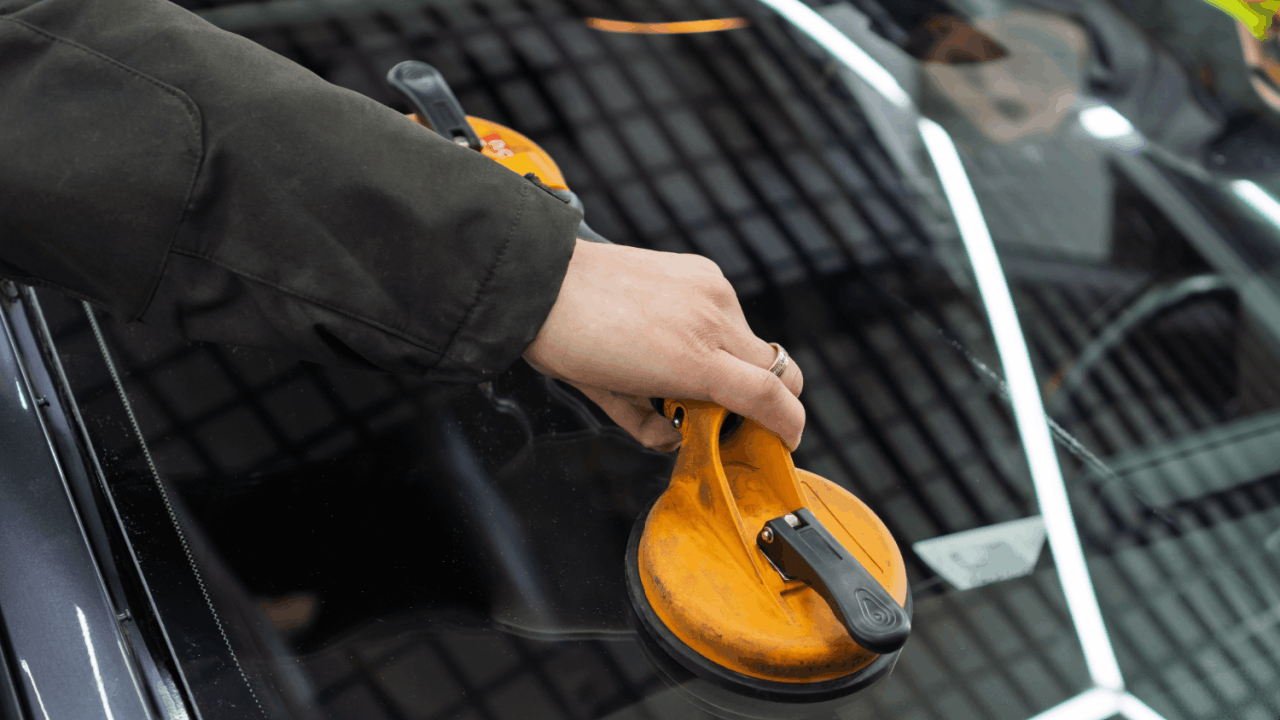 Auto glass repair technician using yellow suction cup tool on car windshield for professional replacement service