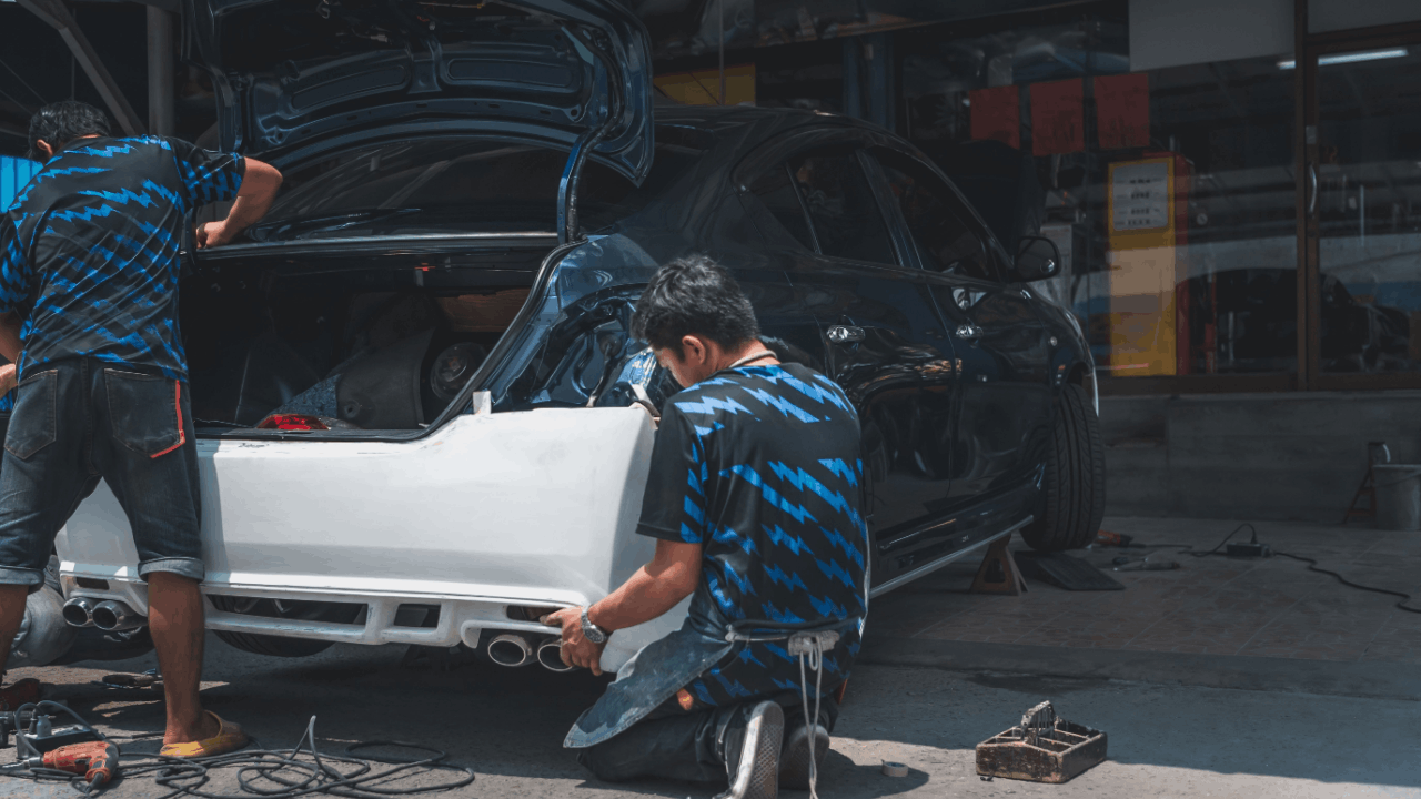 Body shop repair technicians in blue camouflage uniforms working on white sports car with open hood and rear bumper removal