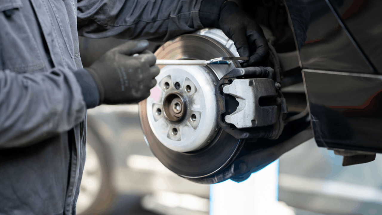 Brake repair mechanic in black gloves inspecting disc rotor and caliper assembly during professional automotive service