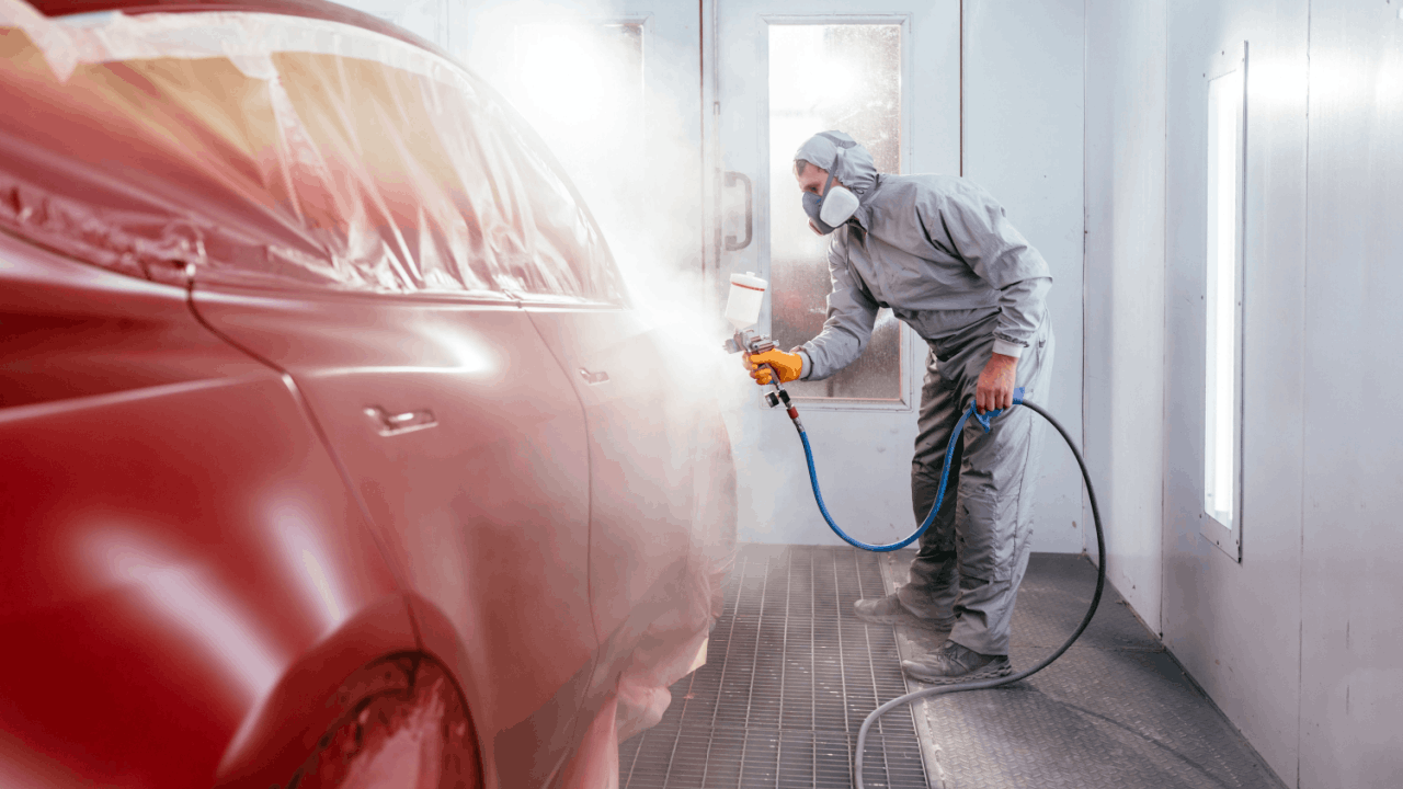 Car body paint professional spray painting red vehicle in automotive paint booth with respirator and protective gear