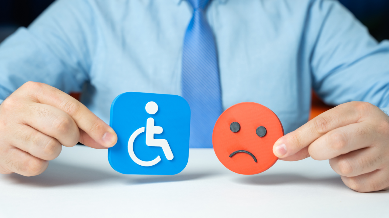 businessman holding wheelchair icon and sad face emoji representing disability discrimination