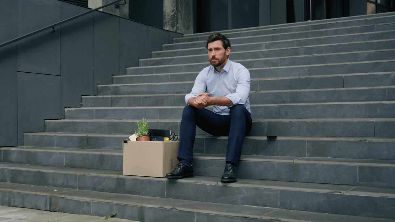 Man sitting on steps after wrongful termination with box of belongings