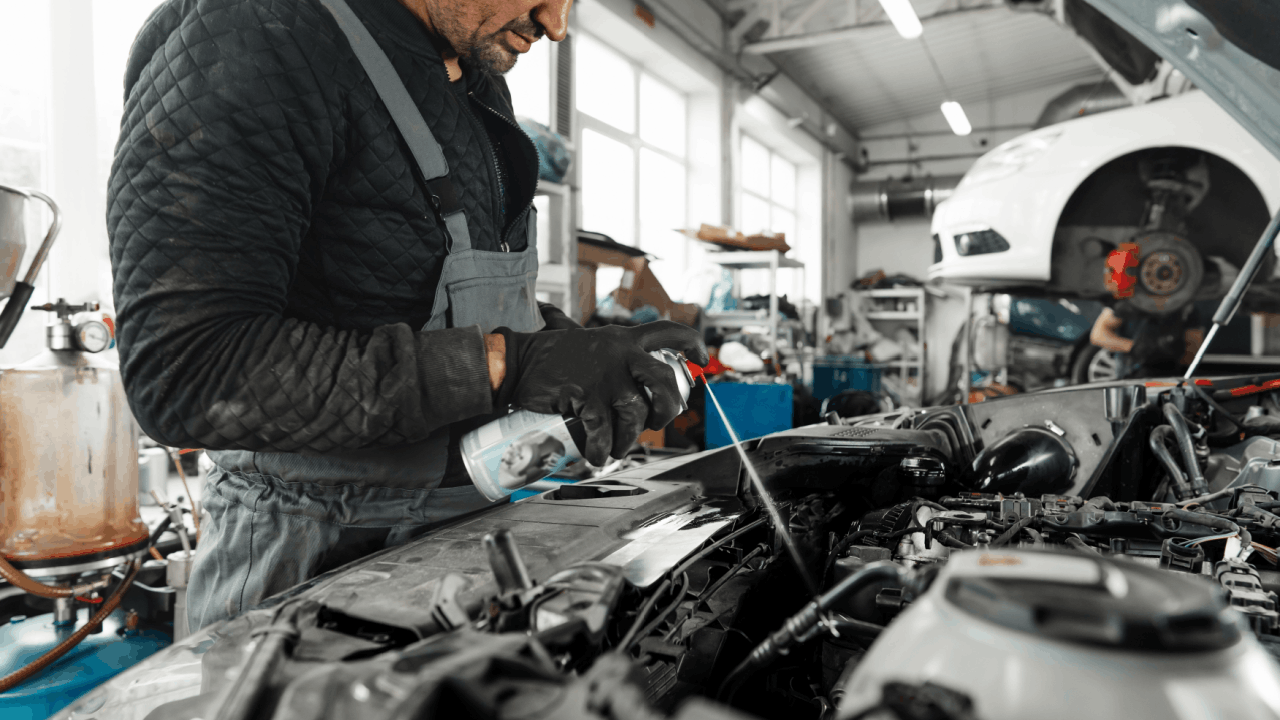 Engine repair mechanic in gray overalls adding fluid to vehicle engine compartment in professional auto shop