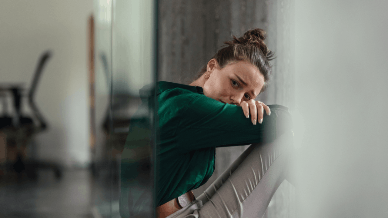 distressed woman sitting alone in office hallway representing workplace discrimination
