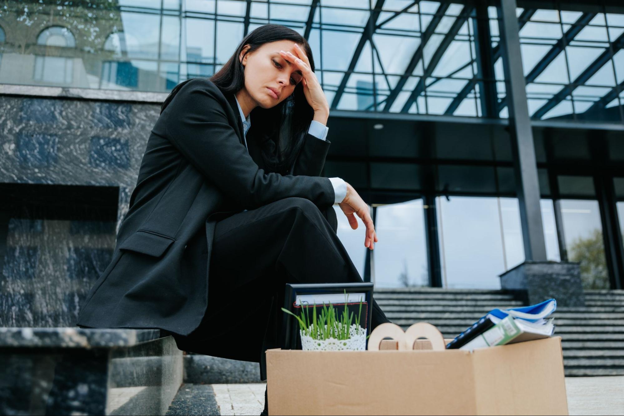 Woman sitting outside office building with box after wrongful firing lawsuit