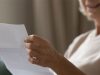 Close up wrinkled female hands holding paper document. Smiling happy middle aged senior woman reading letter, feeling excited by good news