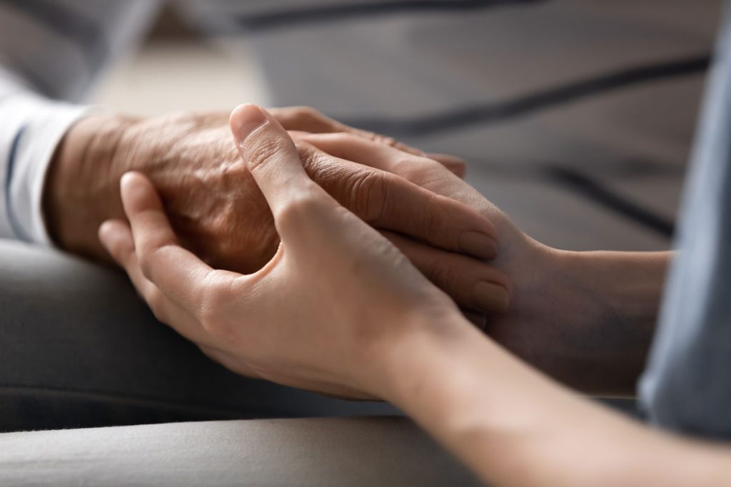 Nurse caregiver or grown up daughter granddaughter holding hand of elderly mother grandma or patient